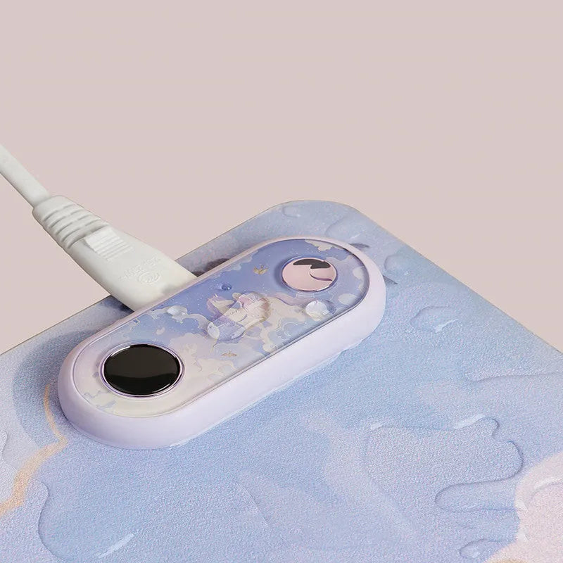 Desktop electric heating pad with patterned PVC leather surface on a wooden desk, plugged into 220V outlet.
