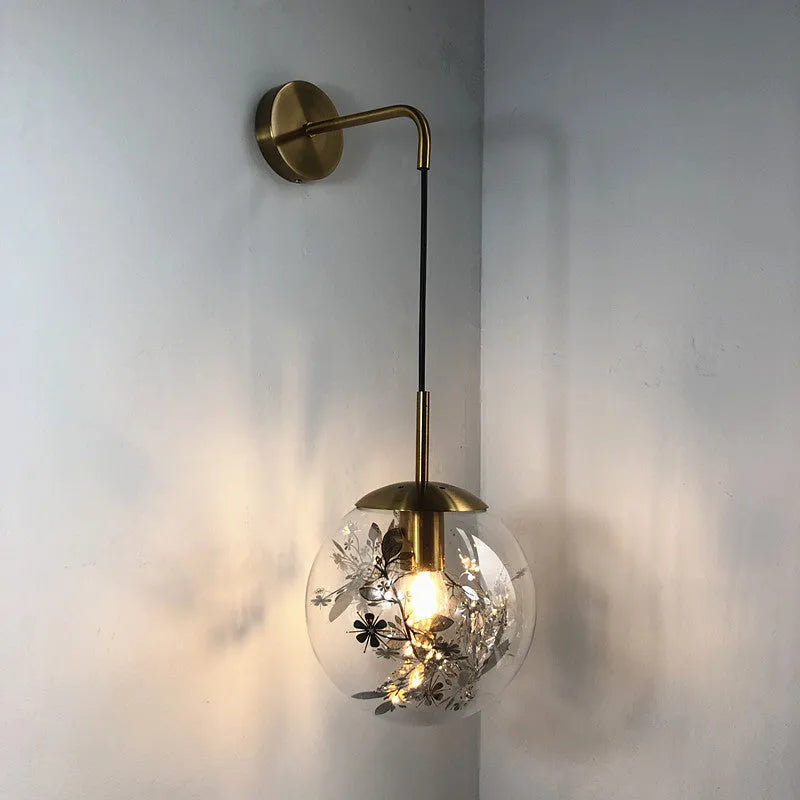 Glass wall lamp with decorative golden flower pattern on a white wall.