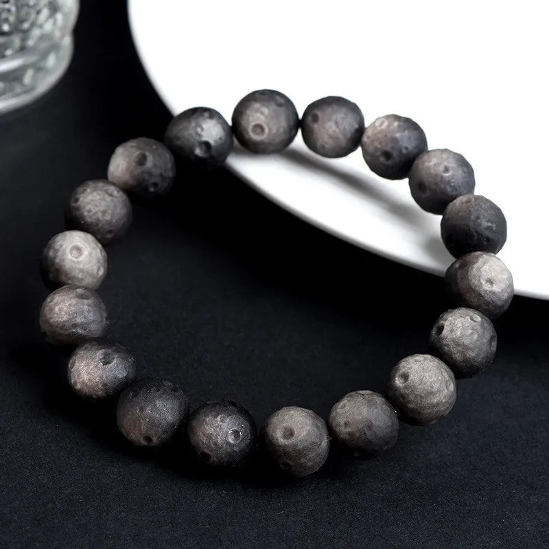 Natural obsidian crater ball bracelet with textured beads in silver stone meteorite colour on a wrist.