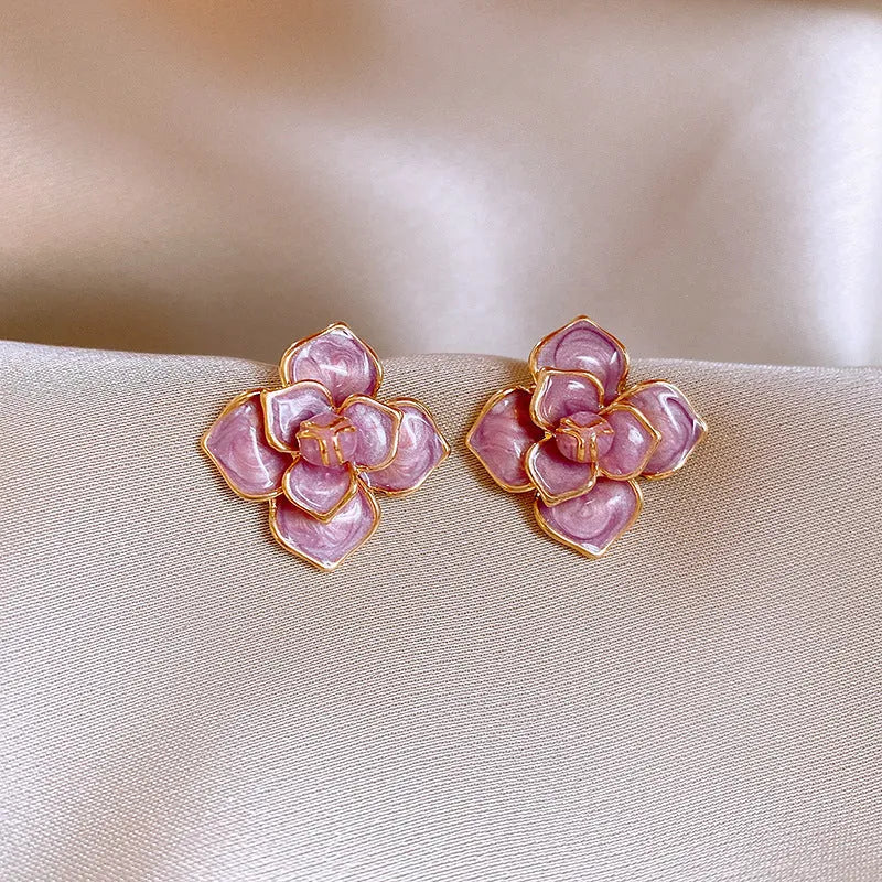 Close-up of a pair of gold plated flower stud earrings with a purple oil-spot glaze finish.