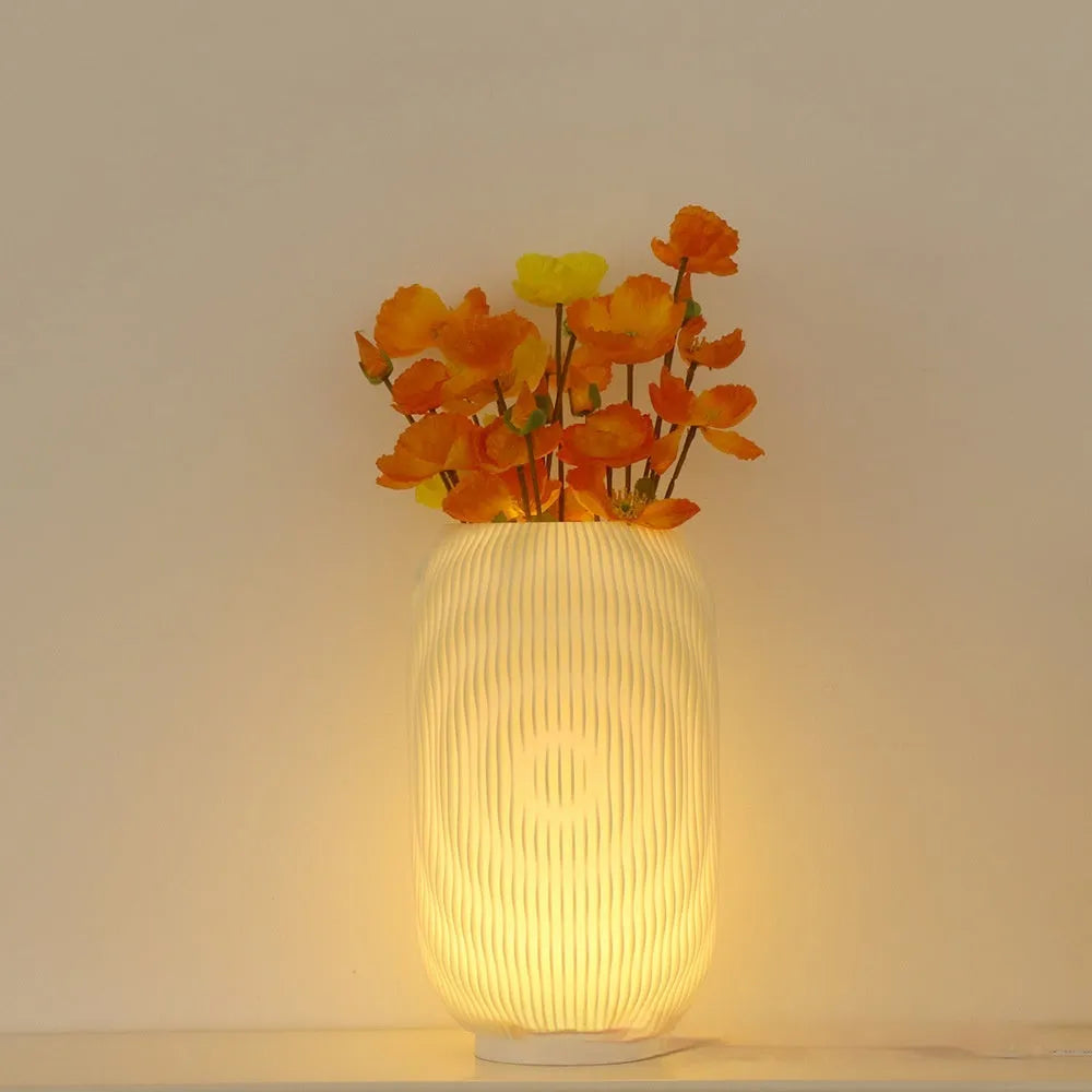 3D printed cylindrical vase night lamp with glass shade in wood colour finish on a bedside table