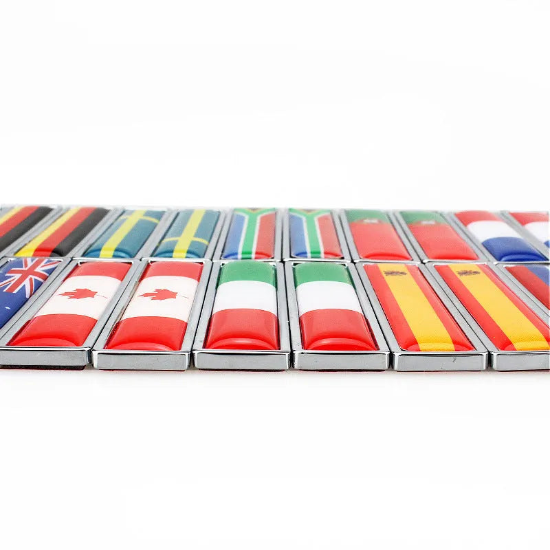 A pair of silver zinc alloy car badge labels with coloured national flag designs, shown at 58mm by 14mm scale.