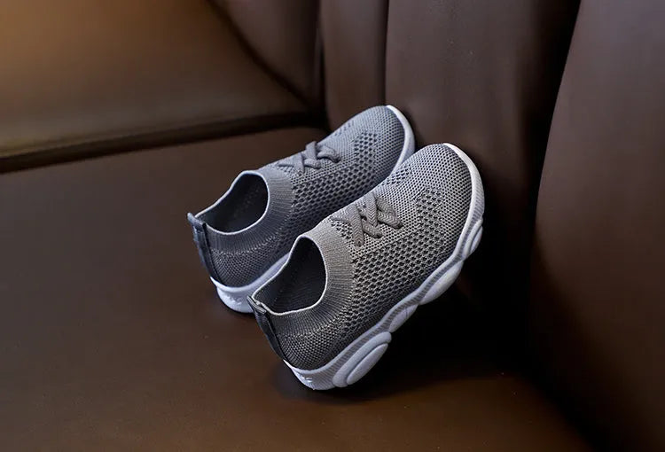 Children's fabric lazy shoe with a non-slip rubber sole, shown in colour options of white, black, pink, and grey.