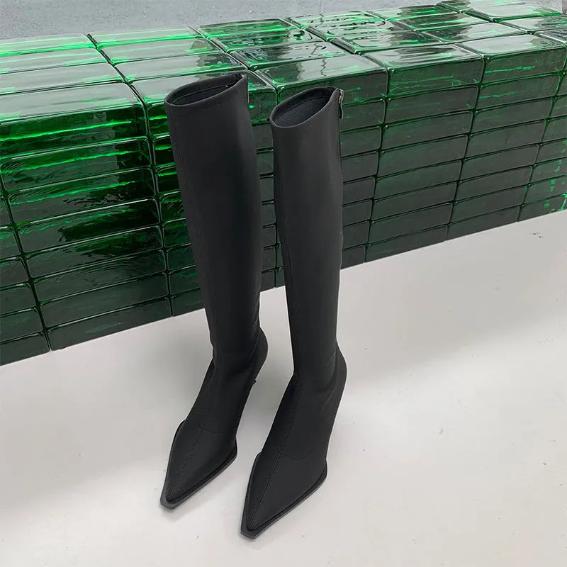 Black women's pointed toe below-the-knee boots with a stiletto heel and back zipper on a plain background.