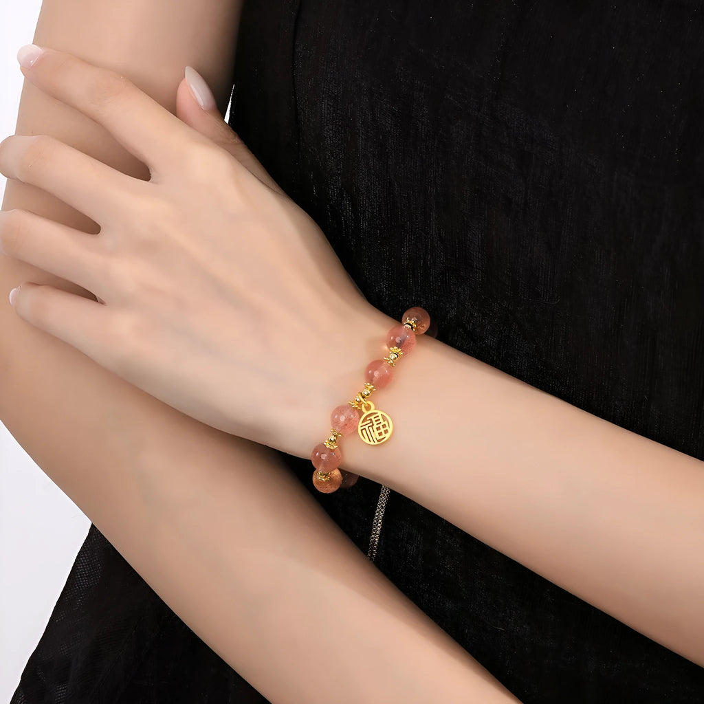 A geometric crystal bracelet in strawberry quartz colour with a fu character detail.