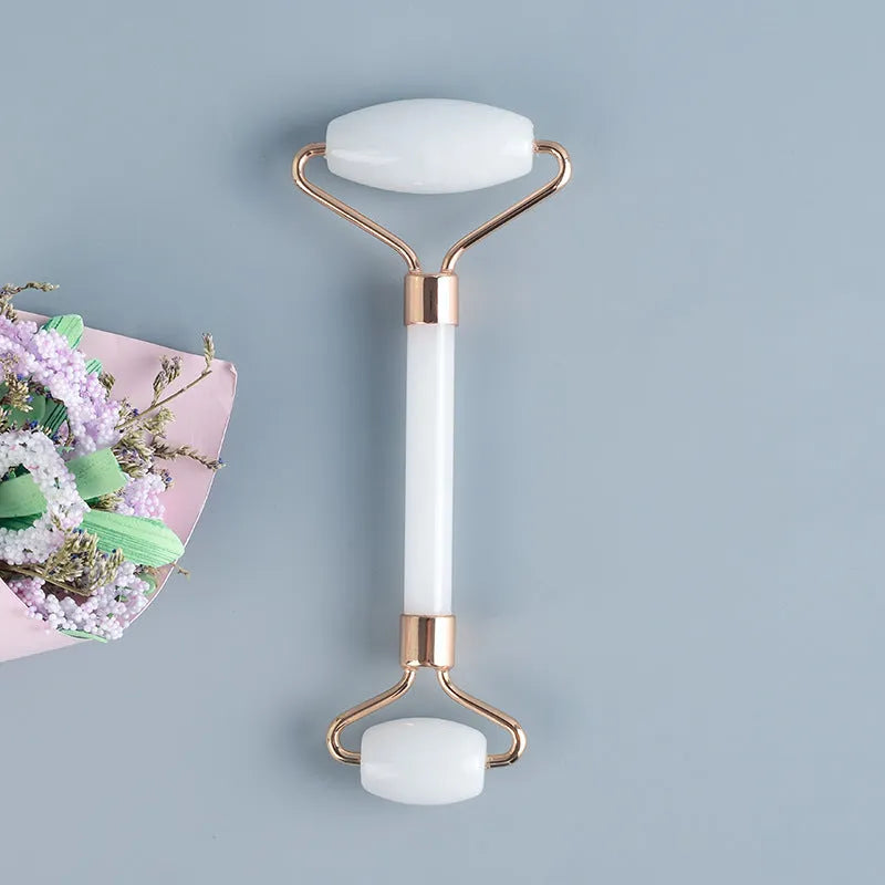 White jade facial roller and gua sha scraper tools placed on a smooth wooden storage board.