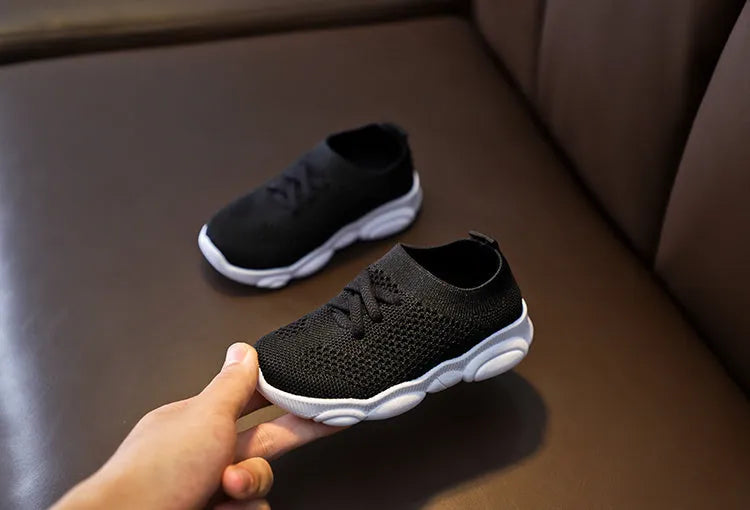 Children's fabric lazy shoe with a non-slip rubber sole, shown in colour options of white, black, pink, and grey.