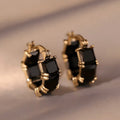 Geometric gold U-shaped hoop earrings with a round black zircon stone, shown from a side view.