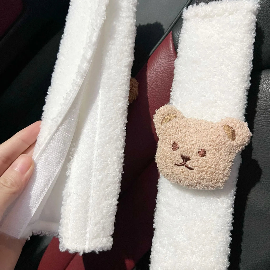 Plush cartoon bear car seat belt shoulder cover in khaki colour, shown next to a car seat.