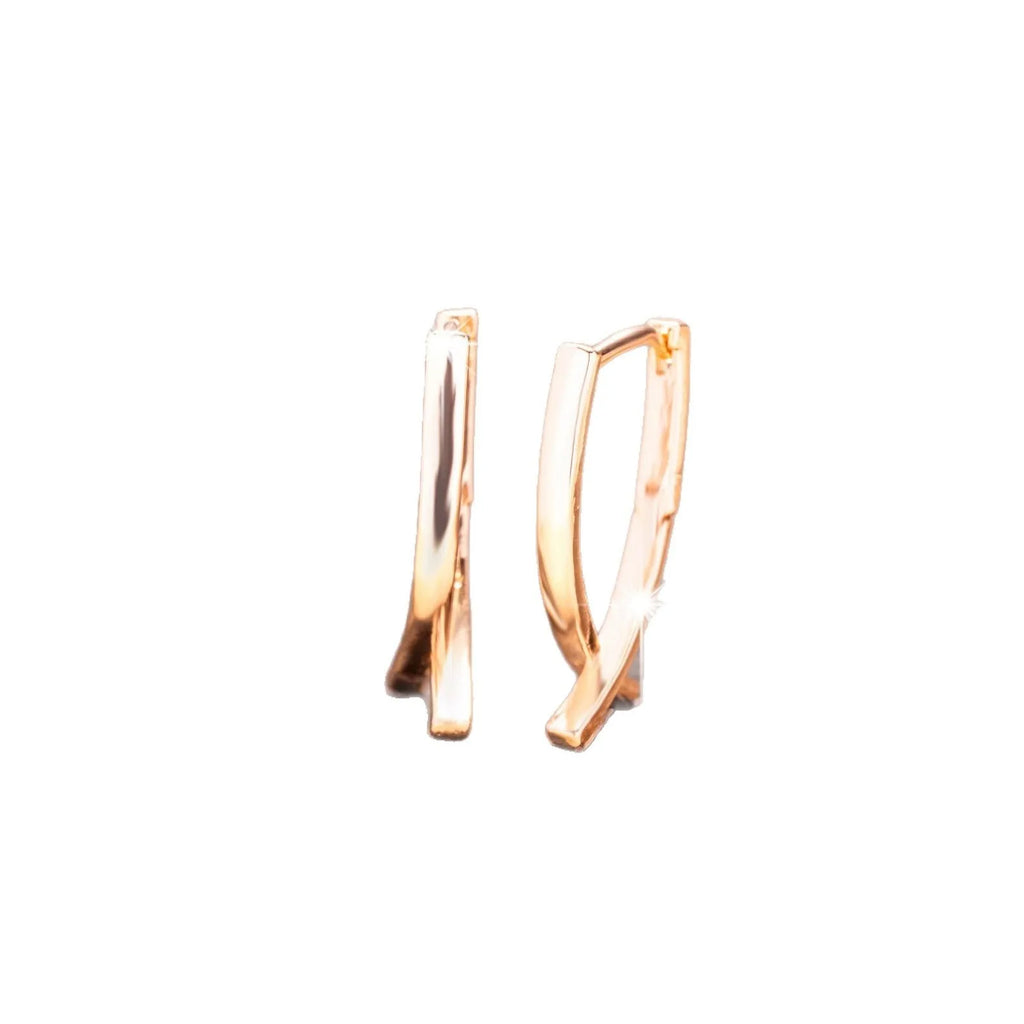 A pair of rose gold coloured cross shaped copper earrings on a plain background.