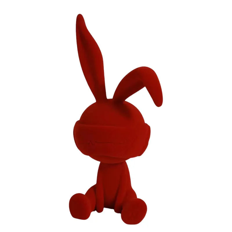 Green resin table ornament of a rabbit wearing a suede blindfold on a wooden shelf.