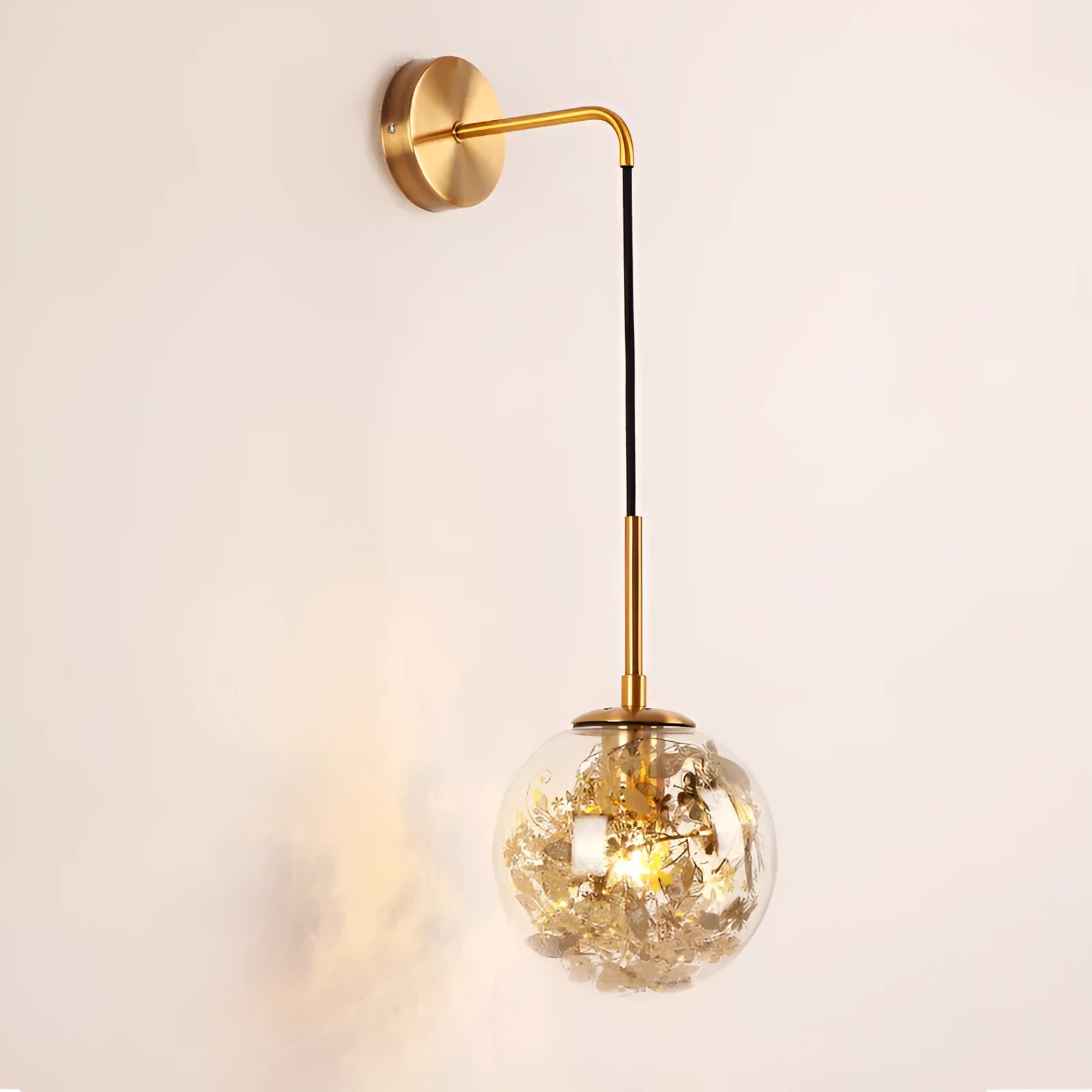 Glass wall lamp with decorative golden flower pattern on a white wall.