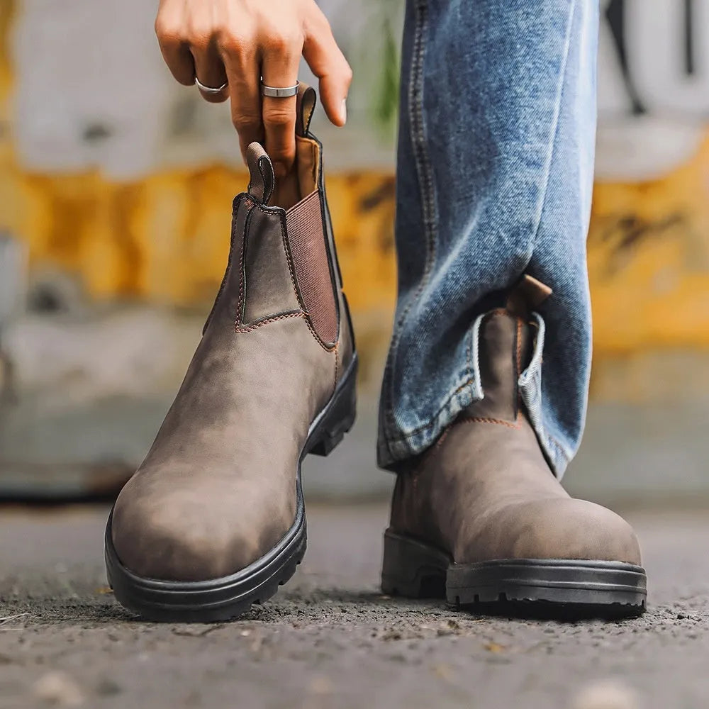 Vintage brown unisex Chelsea boots with round toe and low horseshoe heel on a wooden floor.