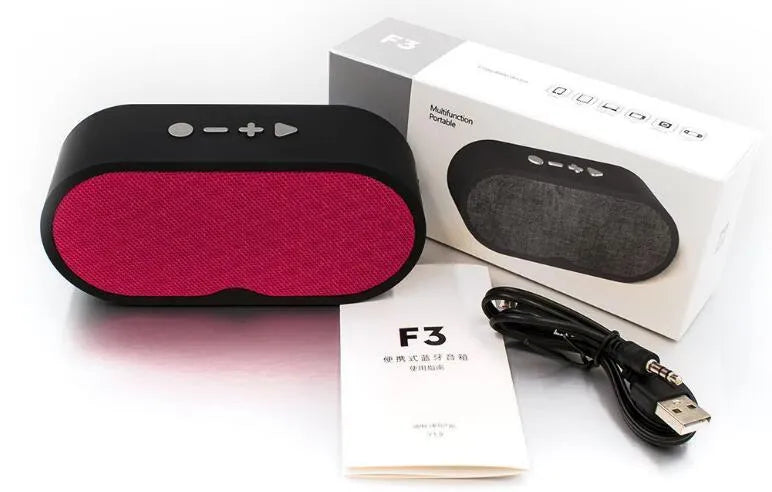 Grey portable Bluetooth speaker with subwoofer, HD microphone, TF card slot and USB port on a table.