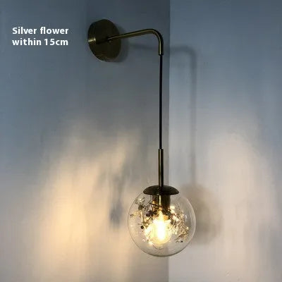 Glass wall lamp with decorative golden flower pattern on a white wall.