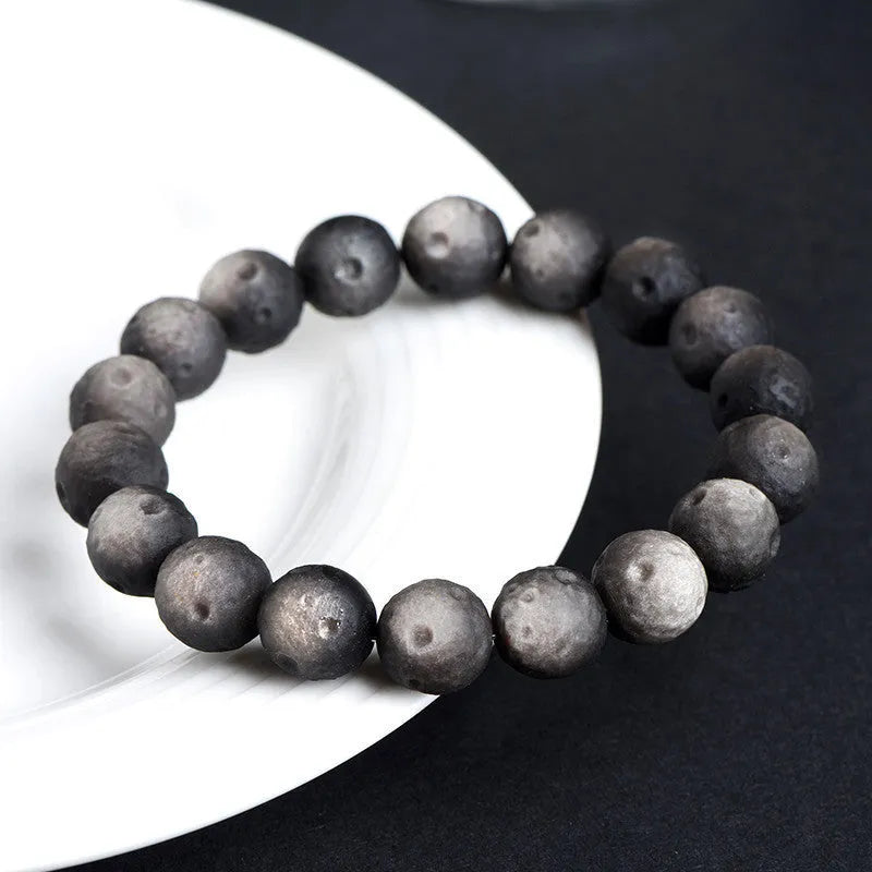 Natural obsidian crater ball bracelet with textured beads in silver stone meteorite colour on a wrist.