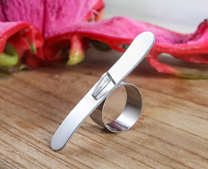 Silver stainless steel fruit peeler ring for oranges, citrus, and pomegranates on a kitchen surface.