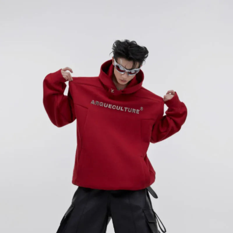 Man wearing a grey hooded sweater with heavy shoulder pads and a detailed 3D metal-effect graphic print.