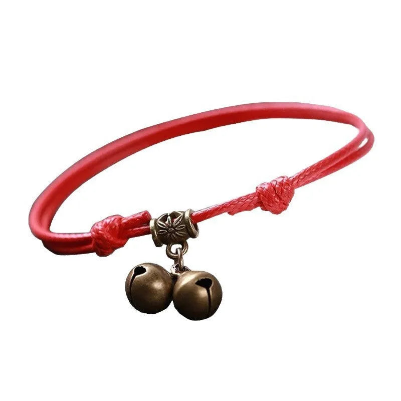 Black nylon rope dog collar with a shiny brass bell on a wooden surface.
