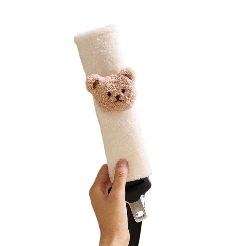 Plush cartoon bear car seat belt shoulder cover in khaki colour, shown next to a car seat.
