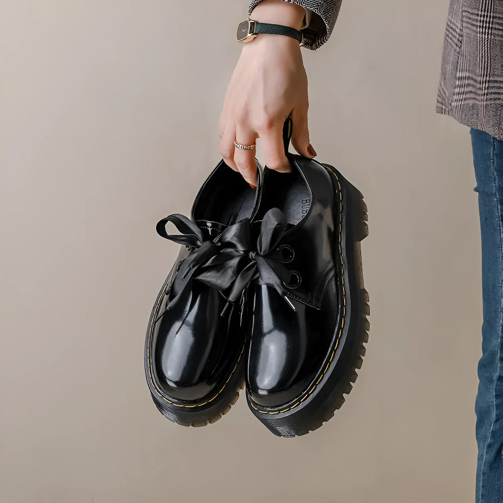 Women's black leather flat shoes with thick soles, cross straps, ribbons, and laced closure.