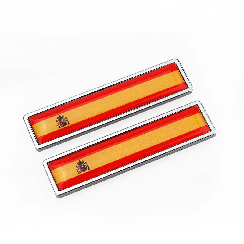 A pair of silver zinc alloy car badge labels with coloured national flag designs, shown at 58mm by 14mm scale.