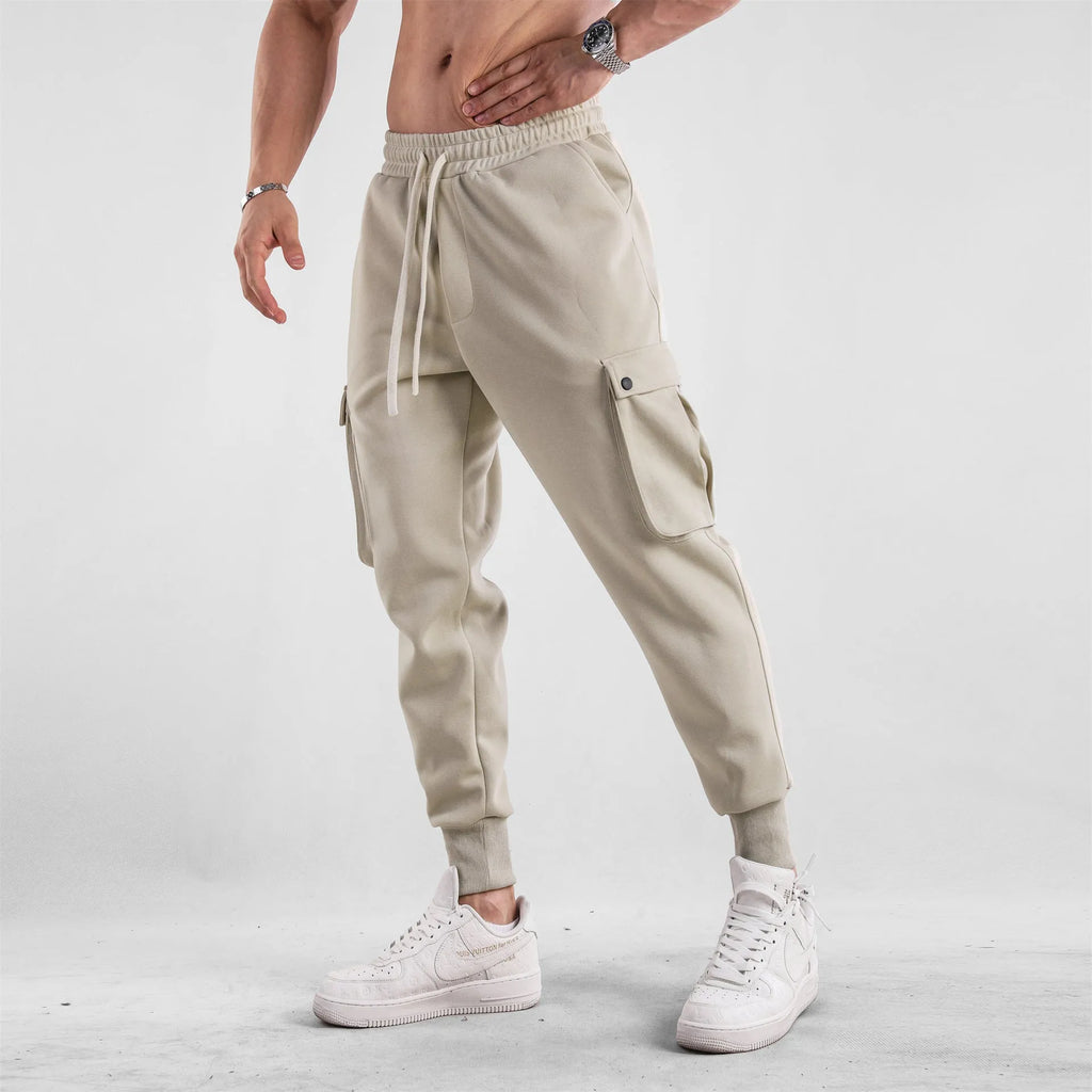 Man wearing loose light grey cotton trousers with ankle-tied cuffs and multiple pockets.