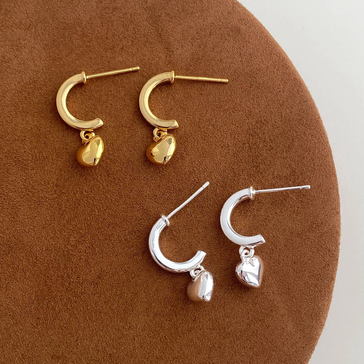Pair of copper heart-shaped C-style earrings in gold electroplated finish on white background