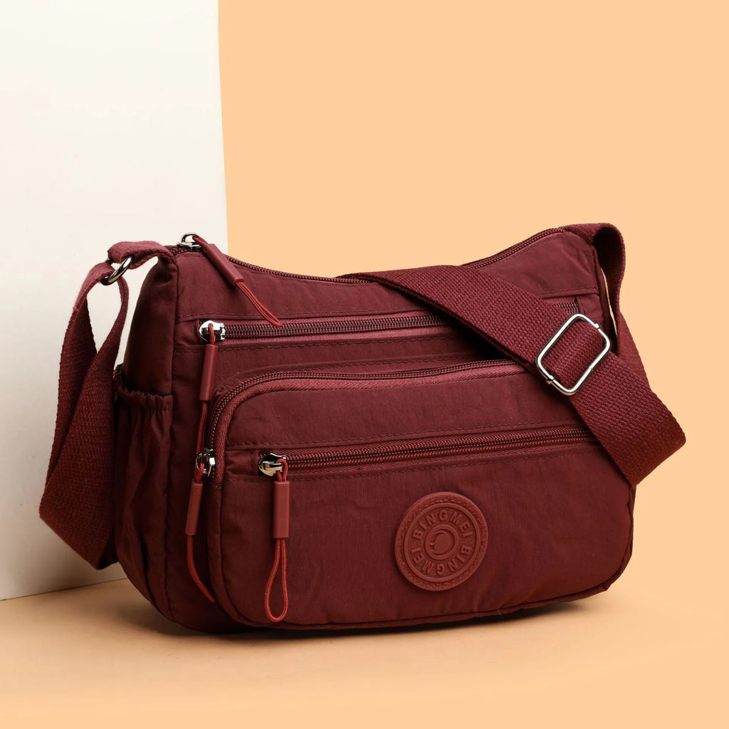 Soft grey nylon crossbody bag with an external pocket and adjustable shoulder strap.