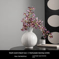 White ceramic ball vase with blue stripes and artificial blue orchid stems on a wooden table.