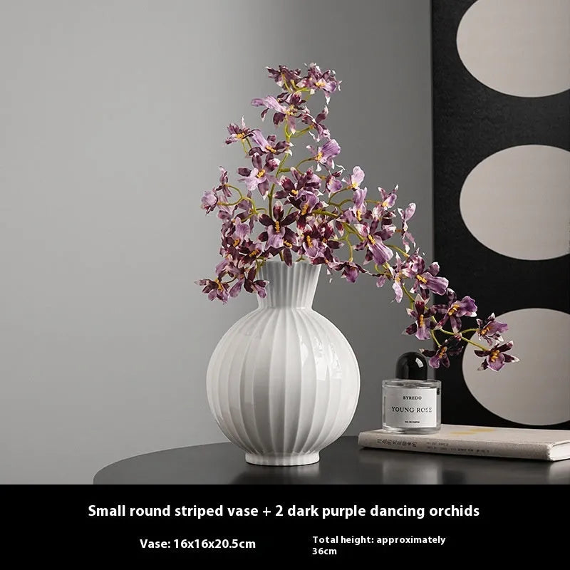 White ceramic ball vase with blue stripes and artificial blue orchid stems on a wooden table.
