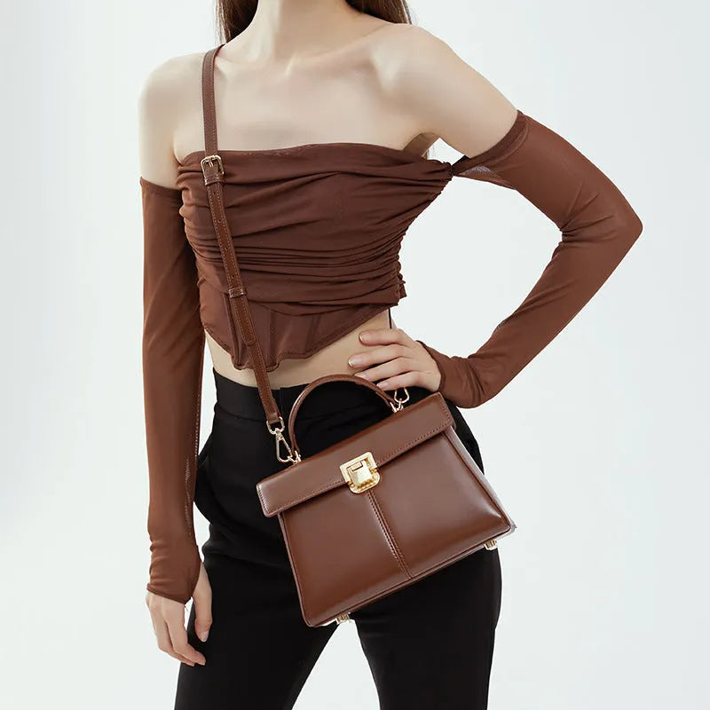 Black leather women's shoulder bag with vachette clasp, shown open to reveal internal zippered pocket.