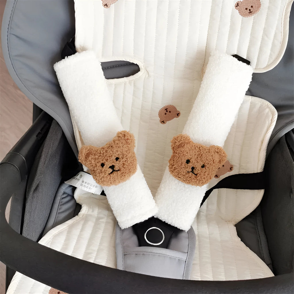 Plush cartoon bear car seat belt shoulder cover in khaki colour, shown next to a car seat.