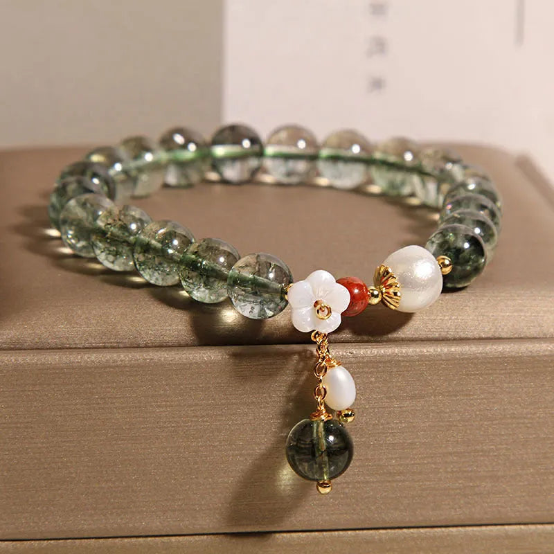 Green phantom quartz crystal bracelet with small shell flower design on woman's wrist.