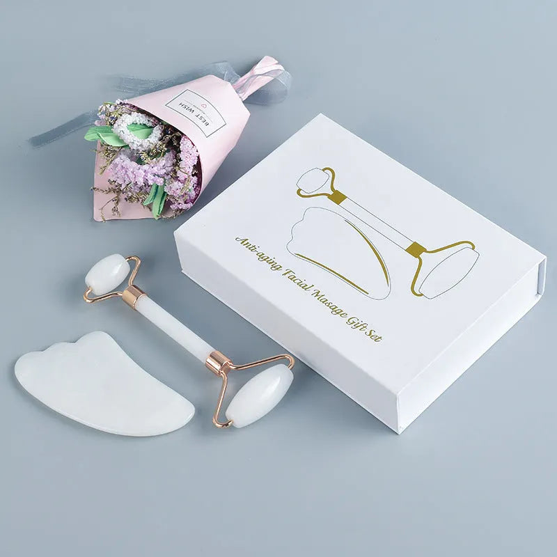 White jade facial roller and gua sha scraper tools placed on a smooth wooden storage board.