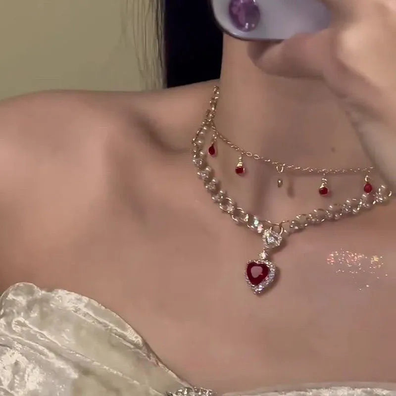 Gold tone double chain necklace with a central red love pearl pendant on an adjustable chain.