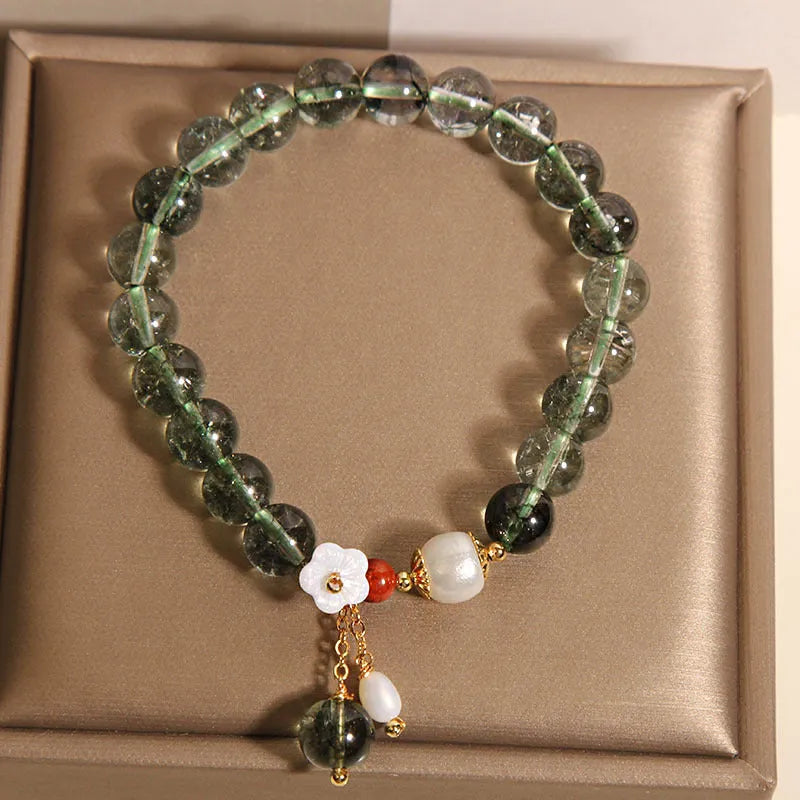 Green phantom quartz crystal bracelet with small shell flower design on woman's wrist.