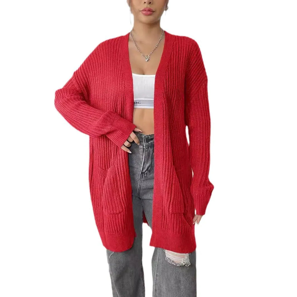 A woman wearing a dark green, loose-fit, mid-length acrylic cardigan with long sleeves and two front pockets.