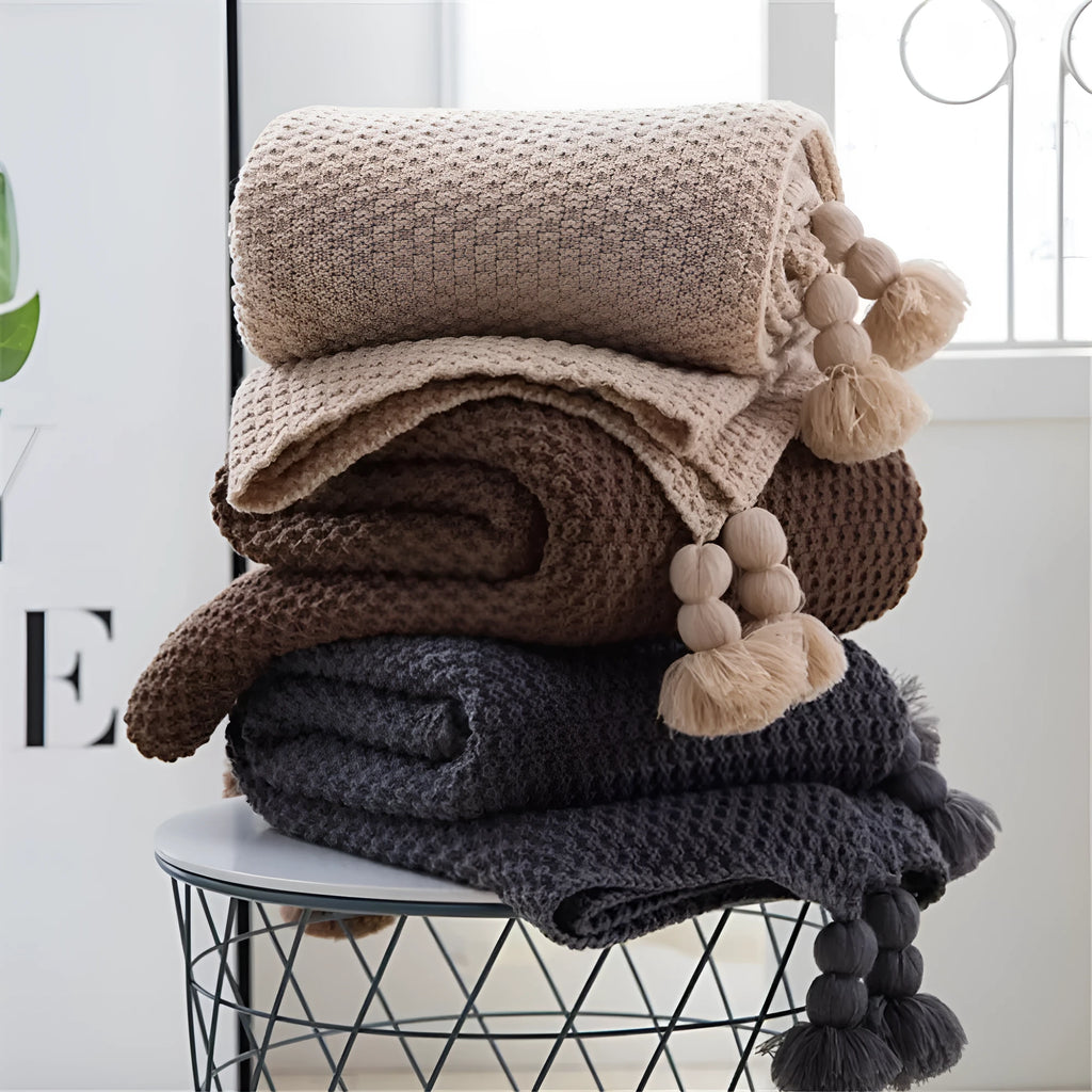 Nordic style knitted acrylic blanket with fringed edges in neutral colour on sofa