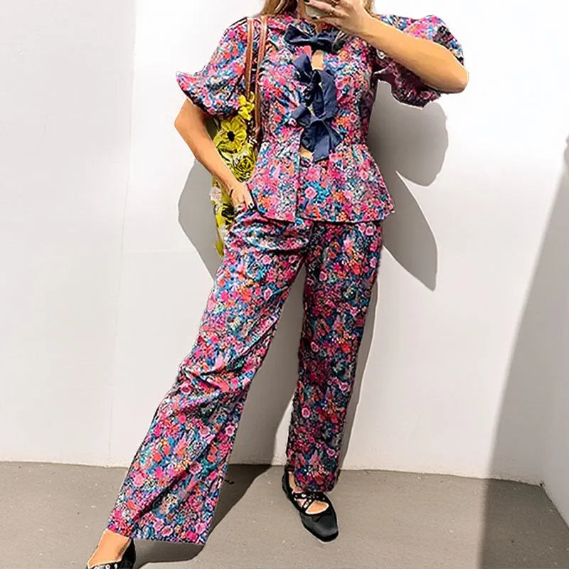 Women's floral print trouser suit set with tie-neck top and puffed sleeves.