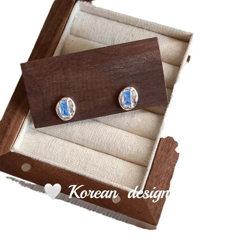 Women's sterling silver earrings with heart-wrapped oval blue diamond centrepiece on silver geometric design