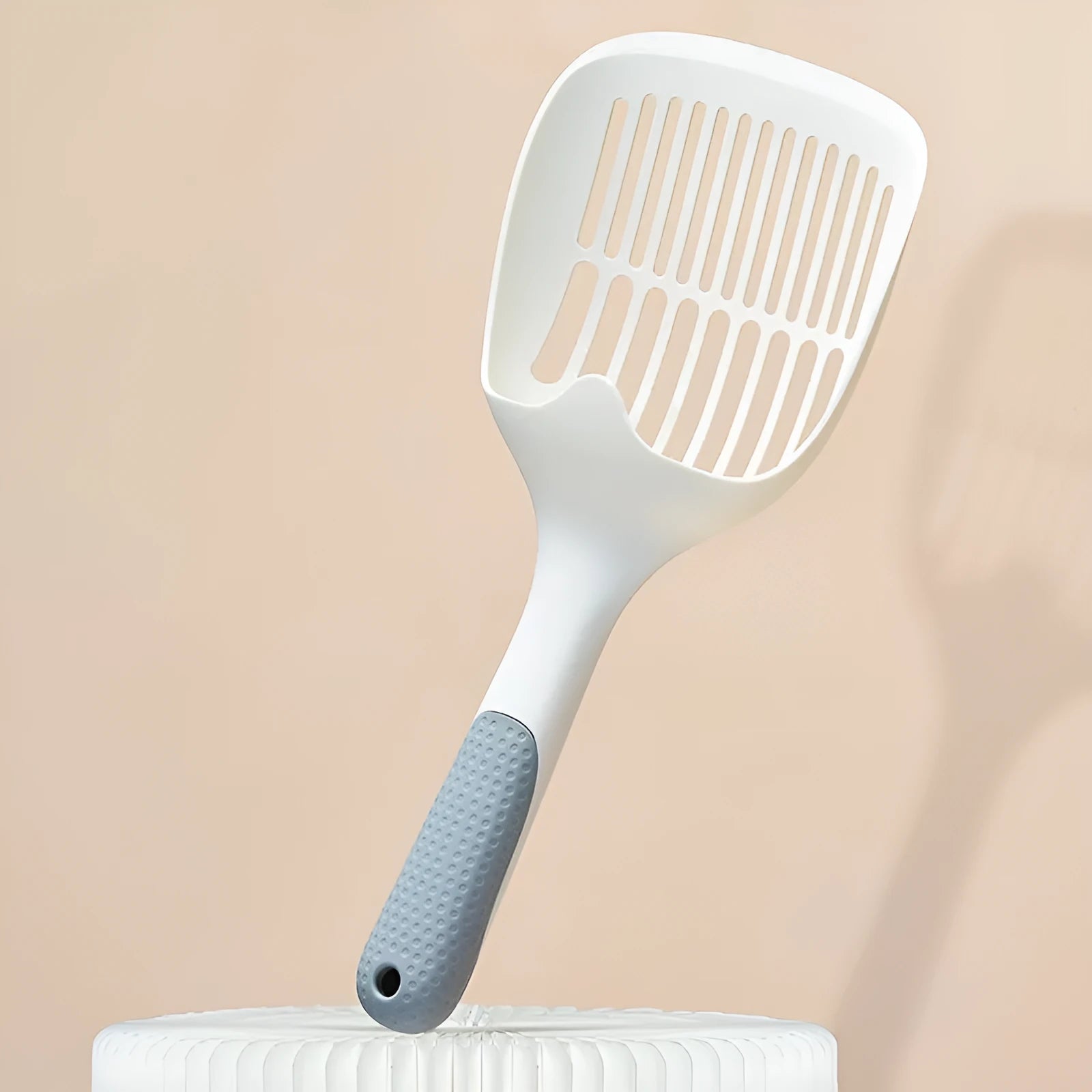 White plastic cat litter scoop with an integrated storage base on a flat surface.