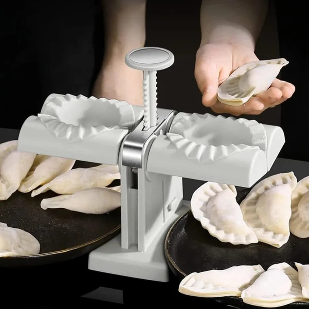 White double-head manual dumpling maker mould made from stainless steel and plastic with an anti-slip base.