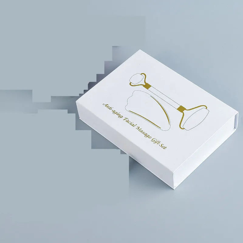 White jade facial roller and gua sha scraper tools placed on a smooth wooden storage board.