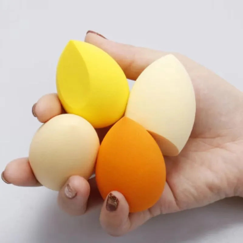 Set of seven differently shaped makeup sponges in various colours on pink background