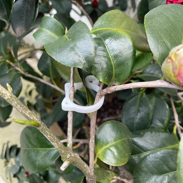 A red plastic cat-shaped plant clip holding a green stem against a garden cane.