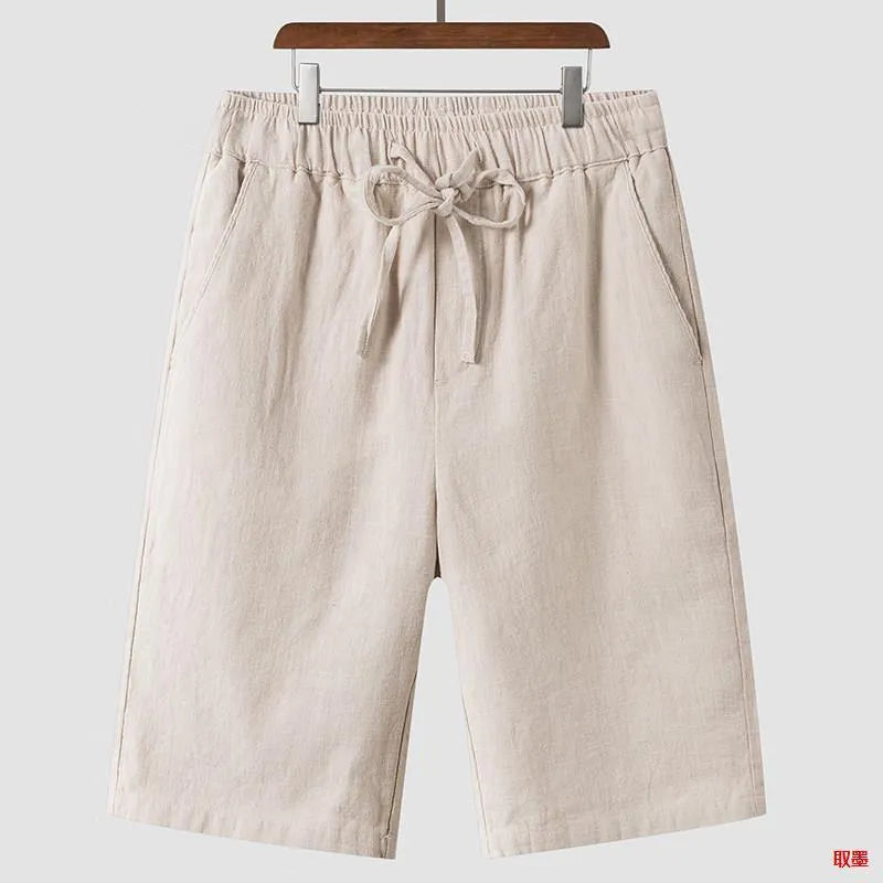 Men's beige linen shorts with loose cropped leg and elasticated waistband on a neutral background.