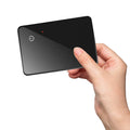 Black credit card-sized pet tracker with wireless charging and a hanging hole, shown next to a coin for scale.