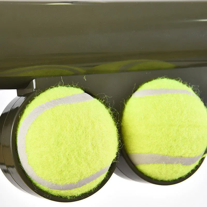 Black ABS plastic tennis ball launcher for dogs with two included tennis balls on grass