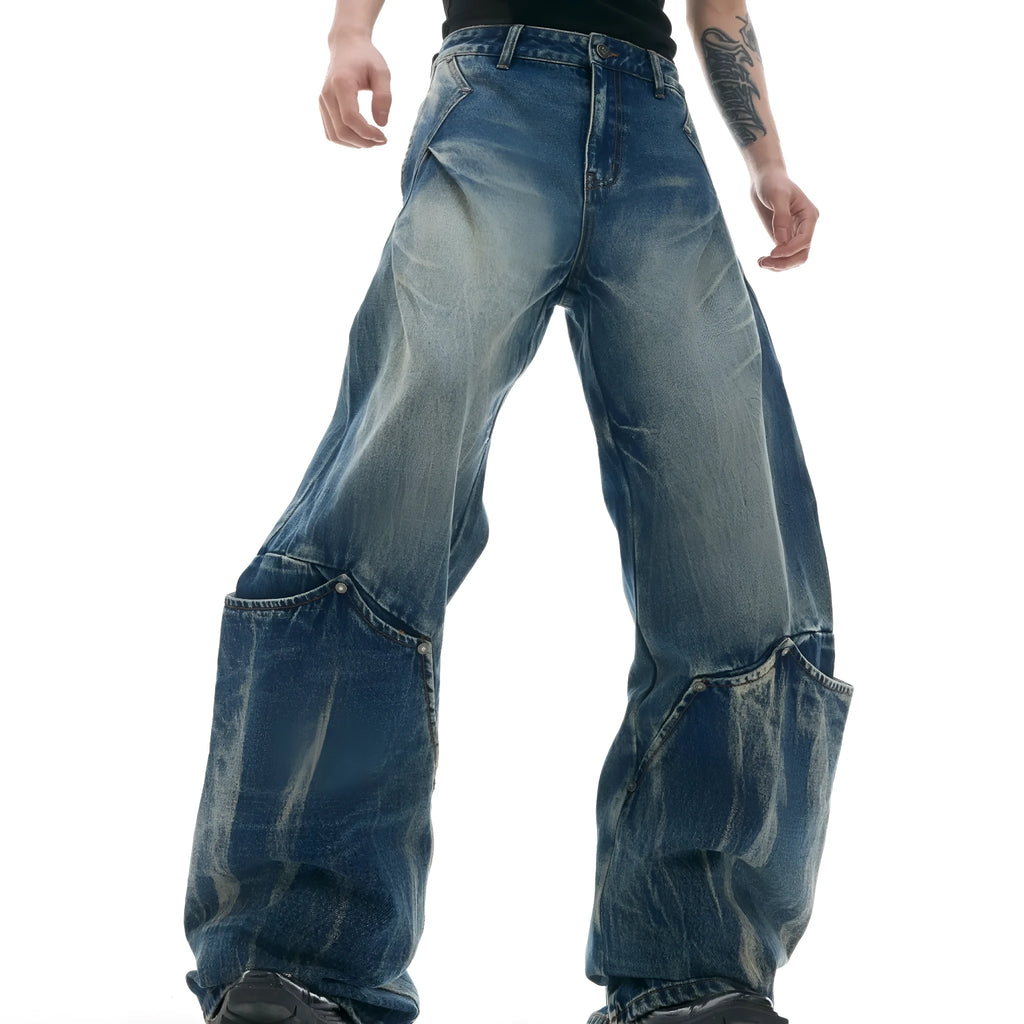 Man wearing loose fit verdant blue retro jeans with a curved knife cut and washed burst pattern.